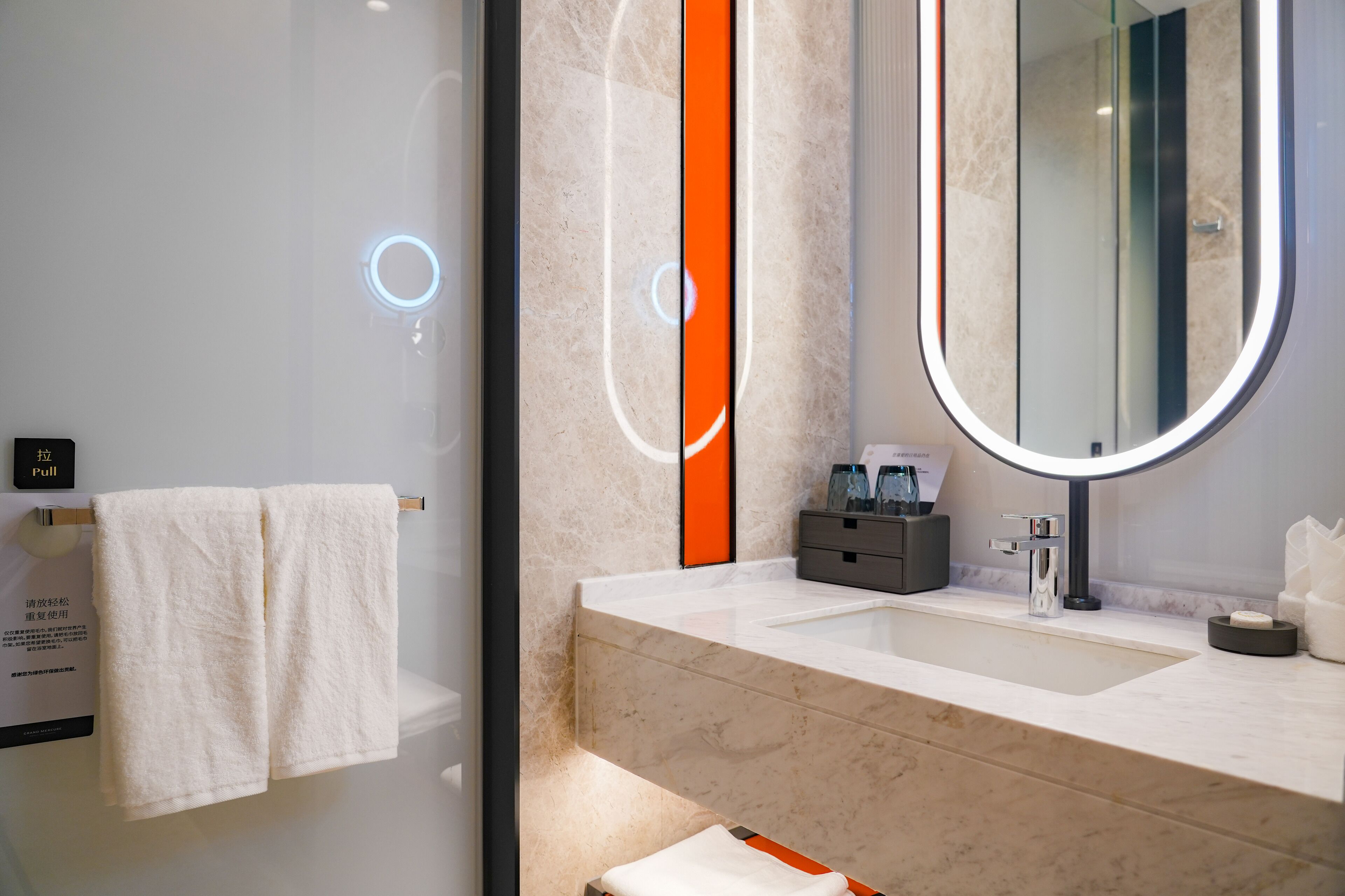 A modern bathroom with a marble sink, a large mirror, and a towel rack.