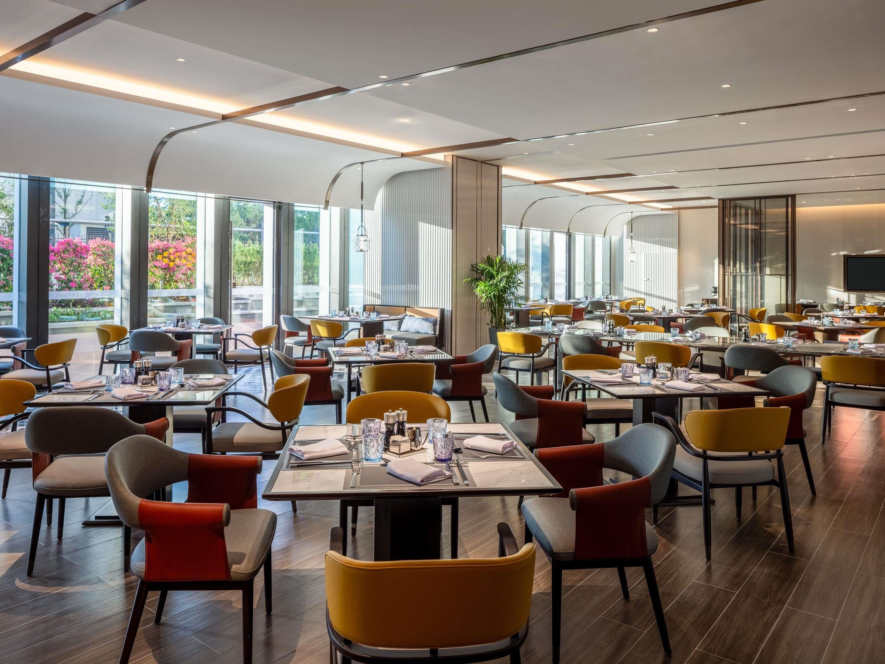 A spacious restaurant with multiple tables and chairs, large windows offering views of the outdoors, and a modern interior design.