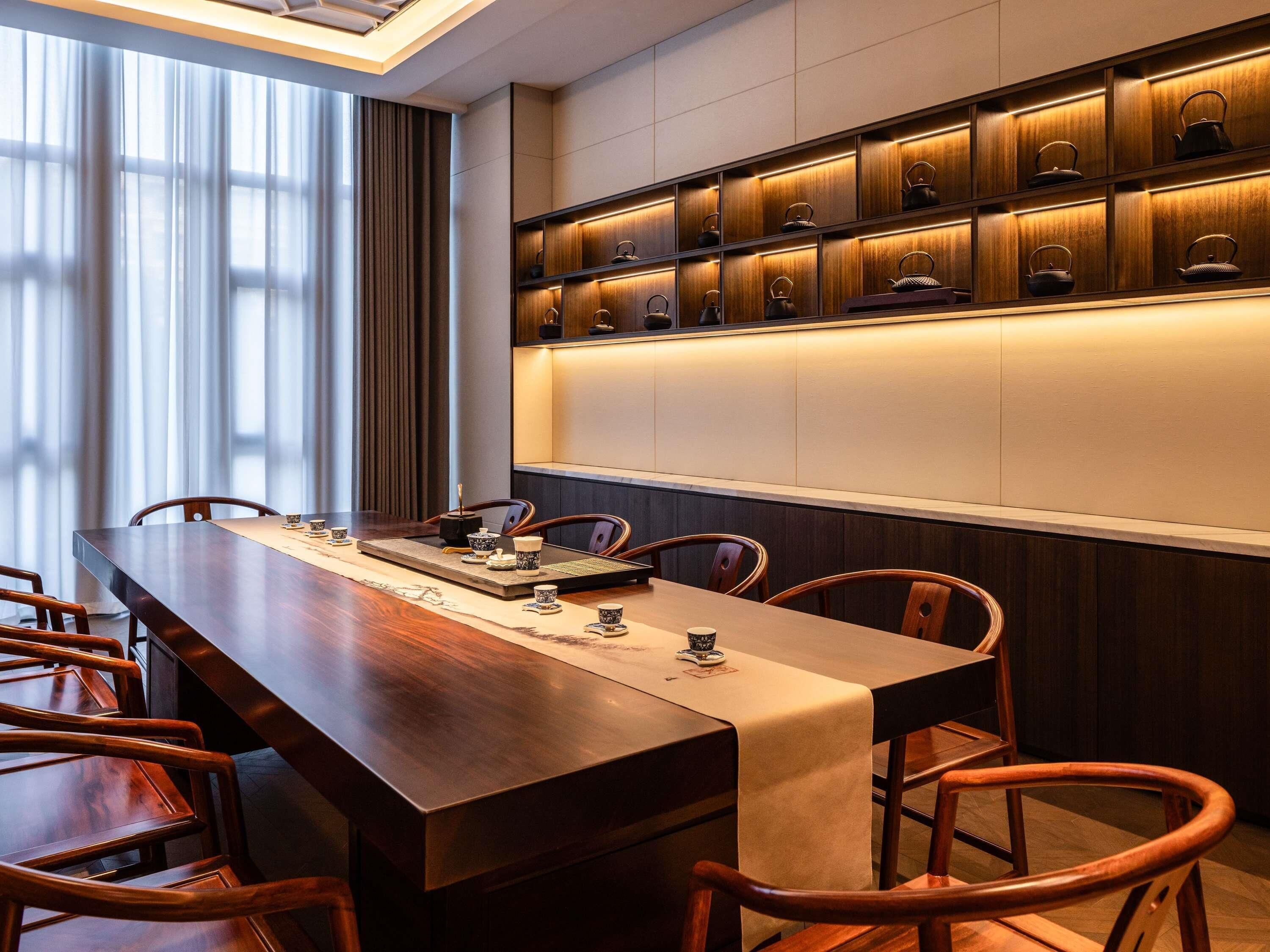 A conference room with a long wooden table, chairs, and a wall-mounted shelf with teapots.