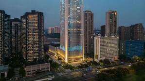 Ein Hochhaus mit moderner Glasfassade, umgeben von weiteren hohen Gebäuden in einer städtischen Umgebung.