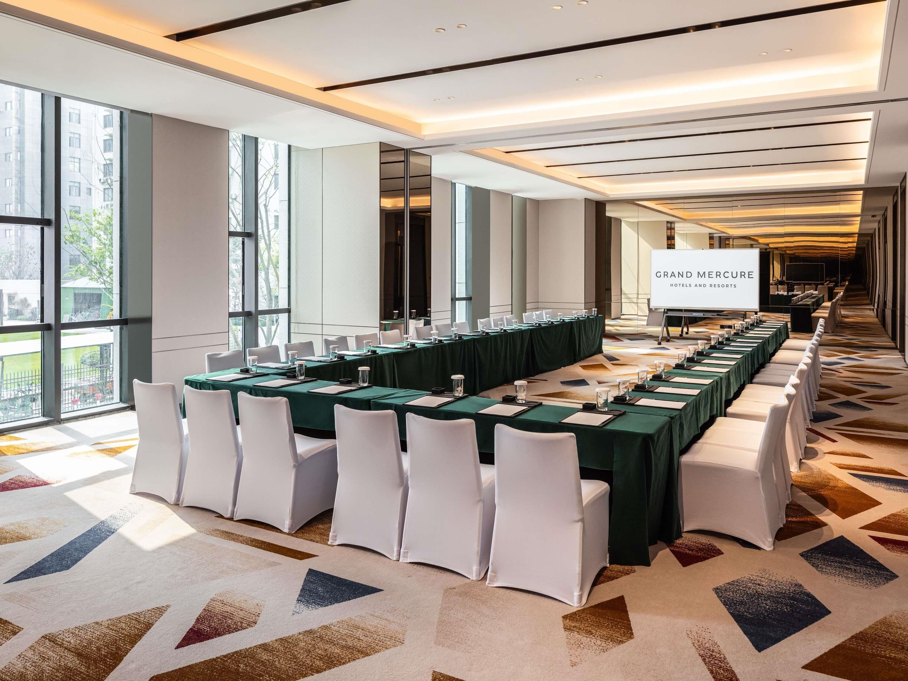 A conference room with a long table, white chairs, and a projector screen displaying 'GRAND MERCURE HOTELS AND RESORTS'.