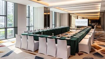 A conference room with a long table, white chairs, and a projector screen displaying 'GRAND MERCURE HOTELS AND RESORTS'.