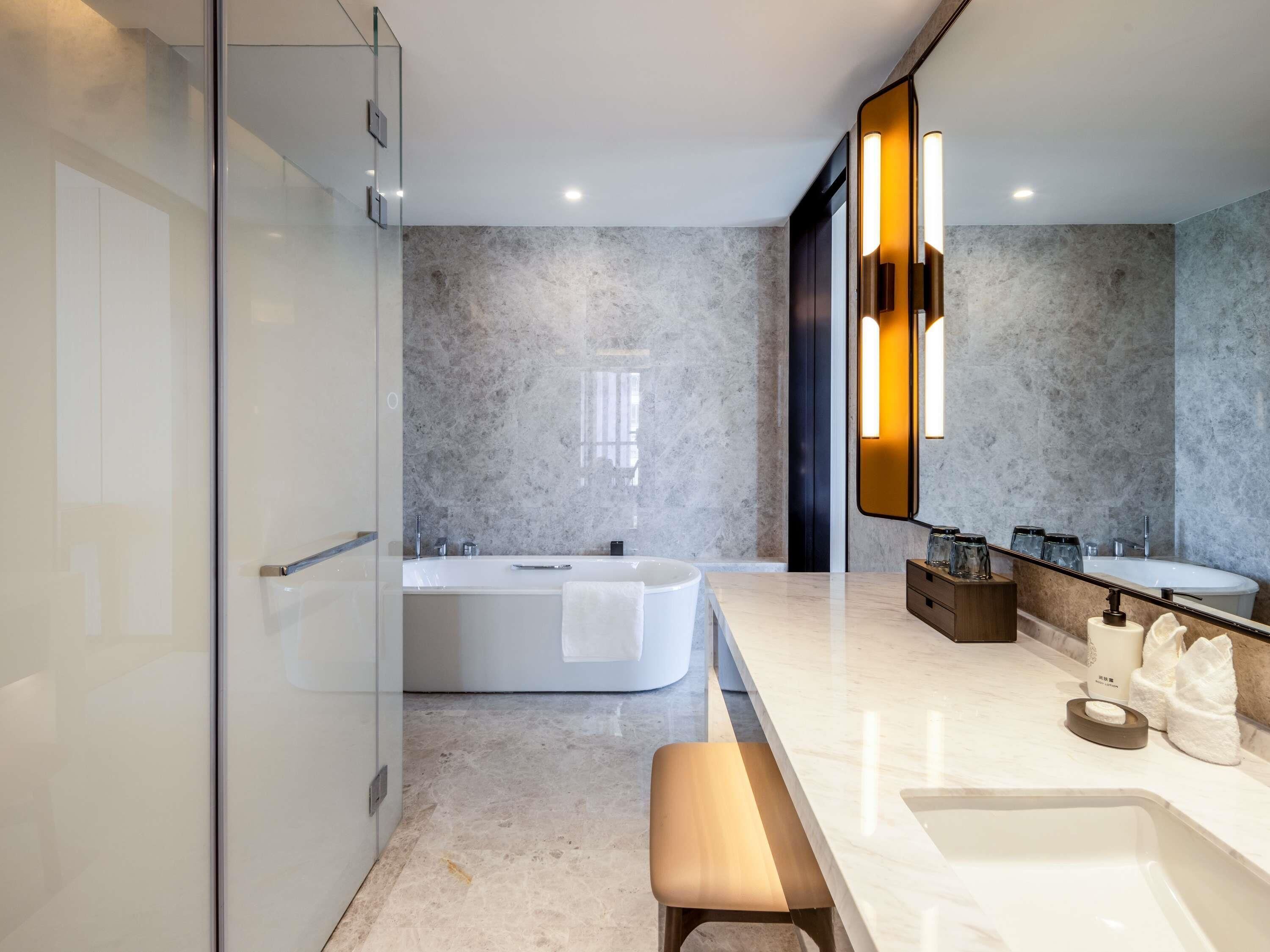 A modern bathroom with a glass shower enclosure, a freestanding bathtub, a vanity with a mirror, and a bench.