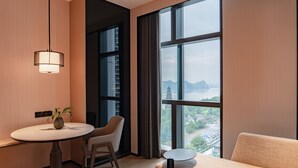 Ein modernes Hotelzimmer mit großem Fenster, einem runden Esstisch, einer Couch und einer Pendelleuchte.