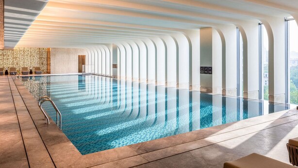 Ein großer, überdachter Schwimmbereich mit klarem, blauem Wasser, umgeben von einem gefliesten Boden und einer Reihe von Rundbögen.
