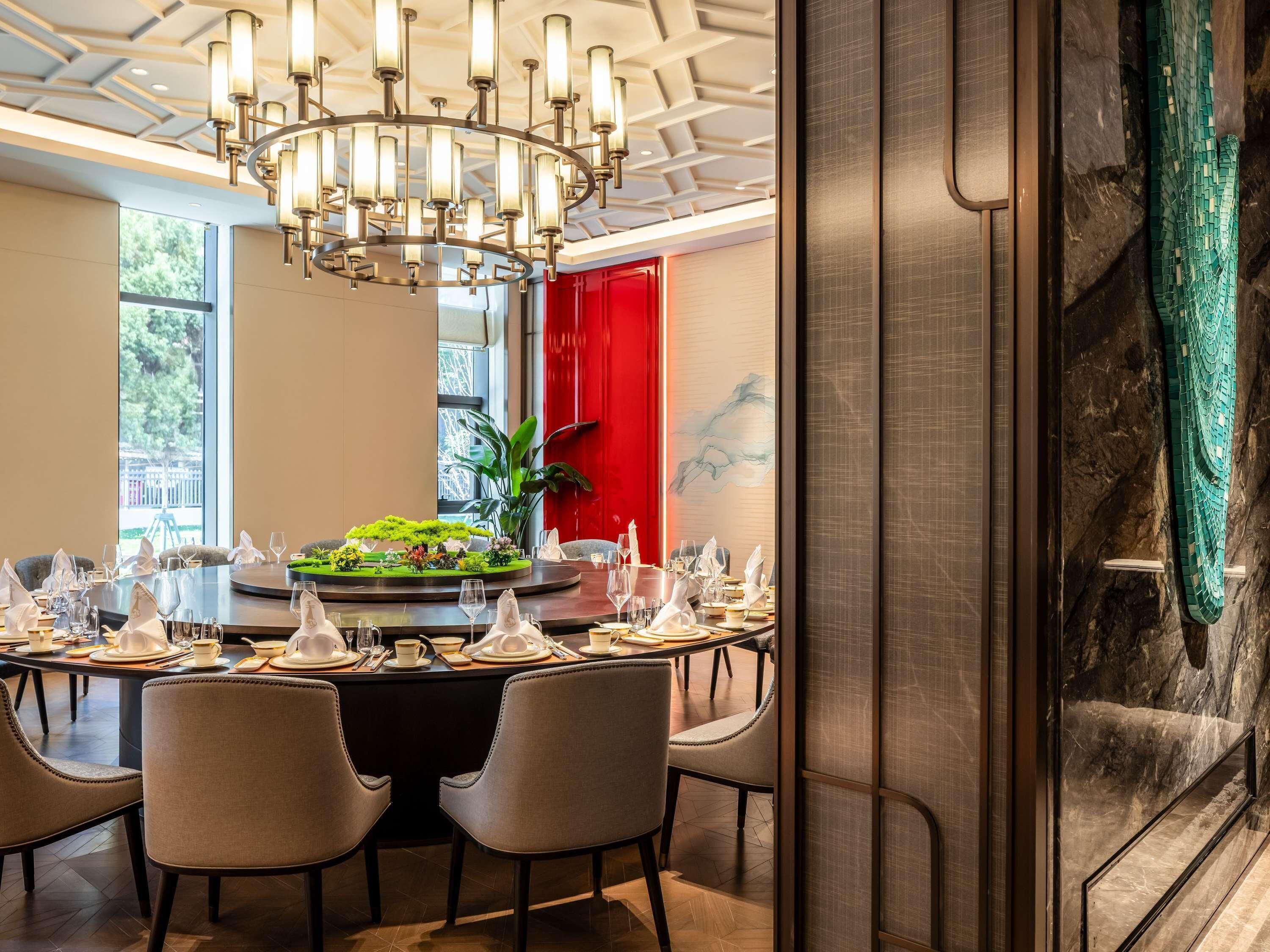 A dining area with a round table set for a meal, surrounded by chairs, with a chandelier overhead and a red accent wall.