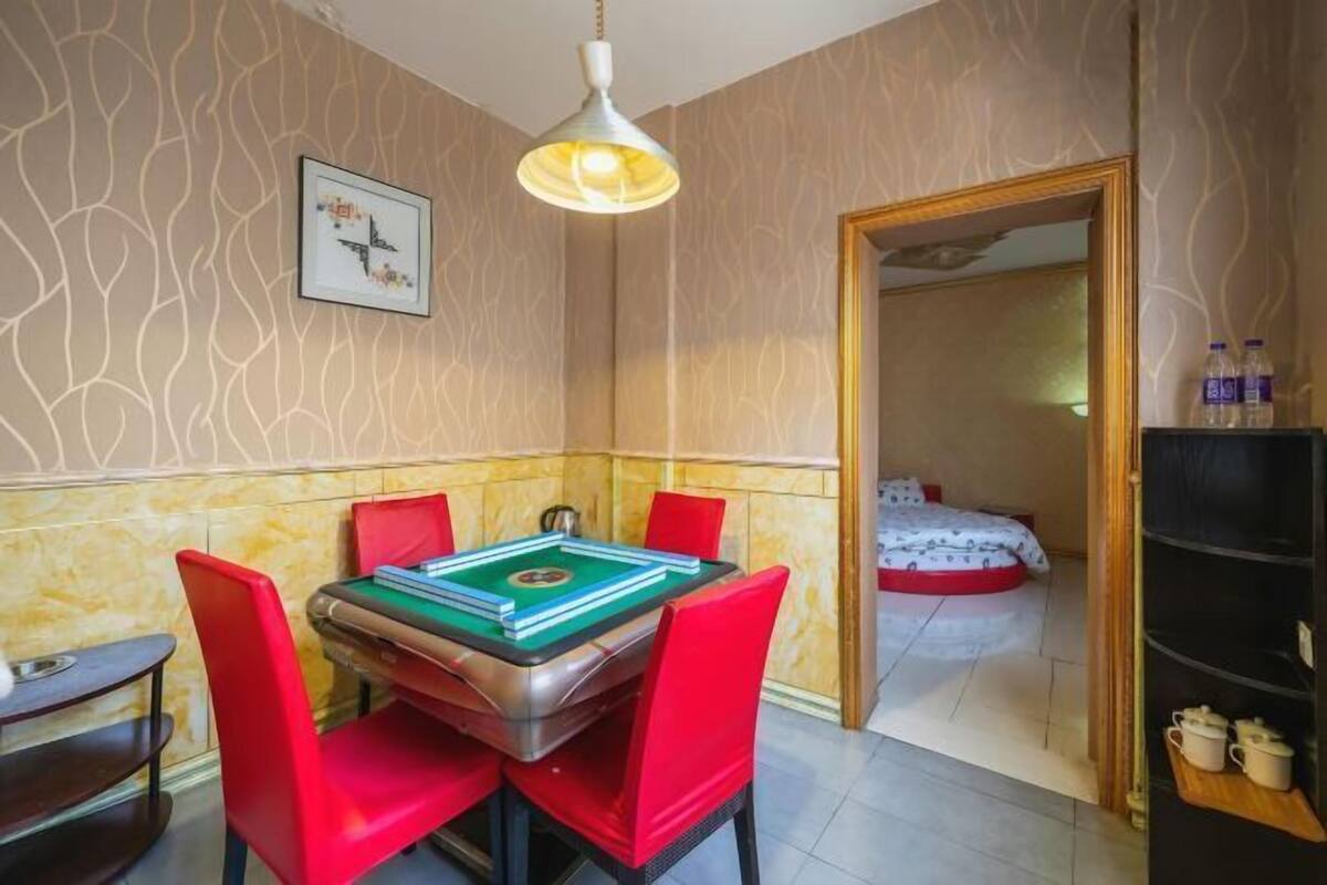 A room with a pool table, red chairs, a bed, and a door leading to another room.