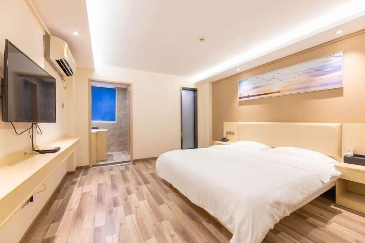 A hotel room with a bed, a television, a painting, and a wooden floor.