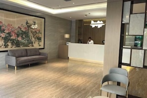 A modern hotel lobby with a reception desk, a sofa, a chair, and a large artwork on the wall. - Fanhua Hotel (Shanghai)
