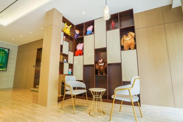 A lobby with a wooden reception desk, two white chairs with gold legs, and a wall decorated with various plush toys. - Fanhua Hotel (Shanghai)