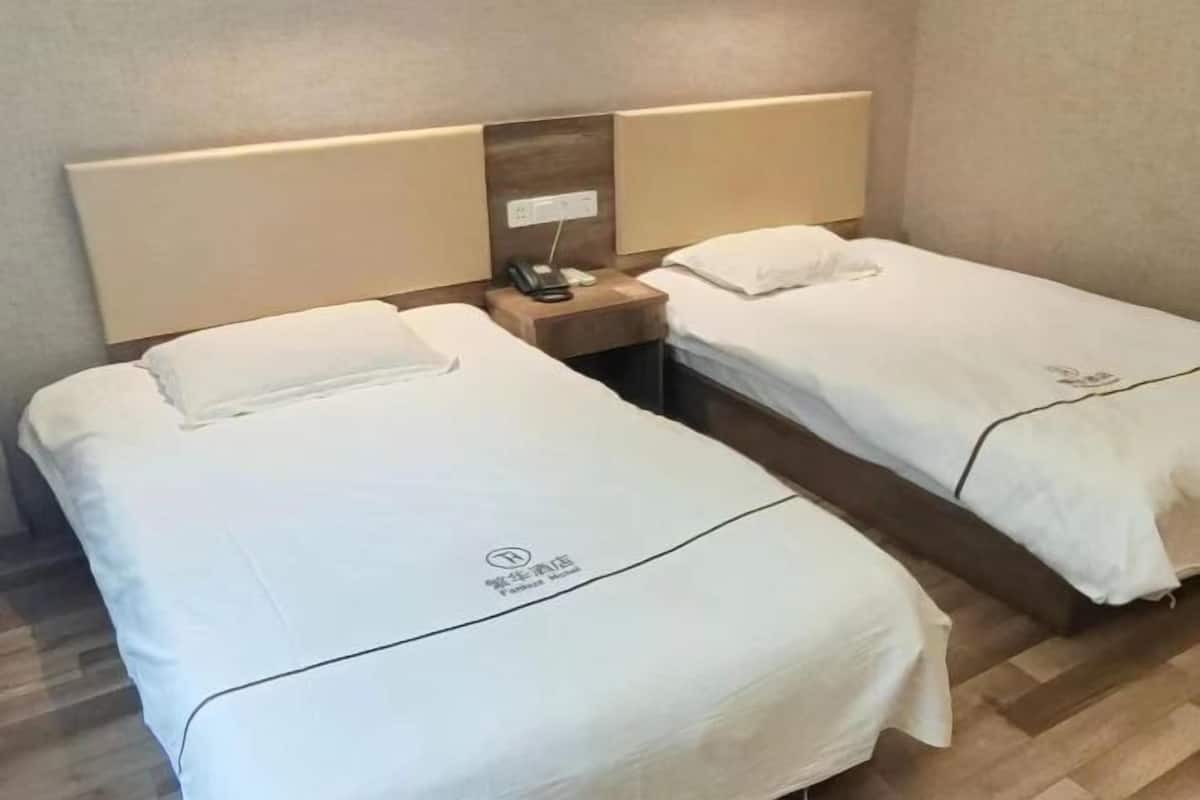 A hotel room with two single beds, each with a wooden headboard and a bedside table.