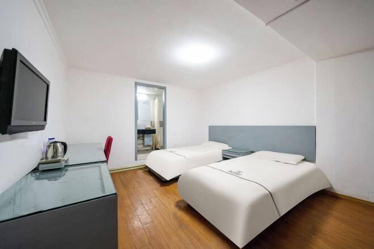 A hotel room with two beds, a TV, a desk with a kettle, and a mirror.