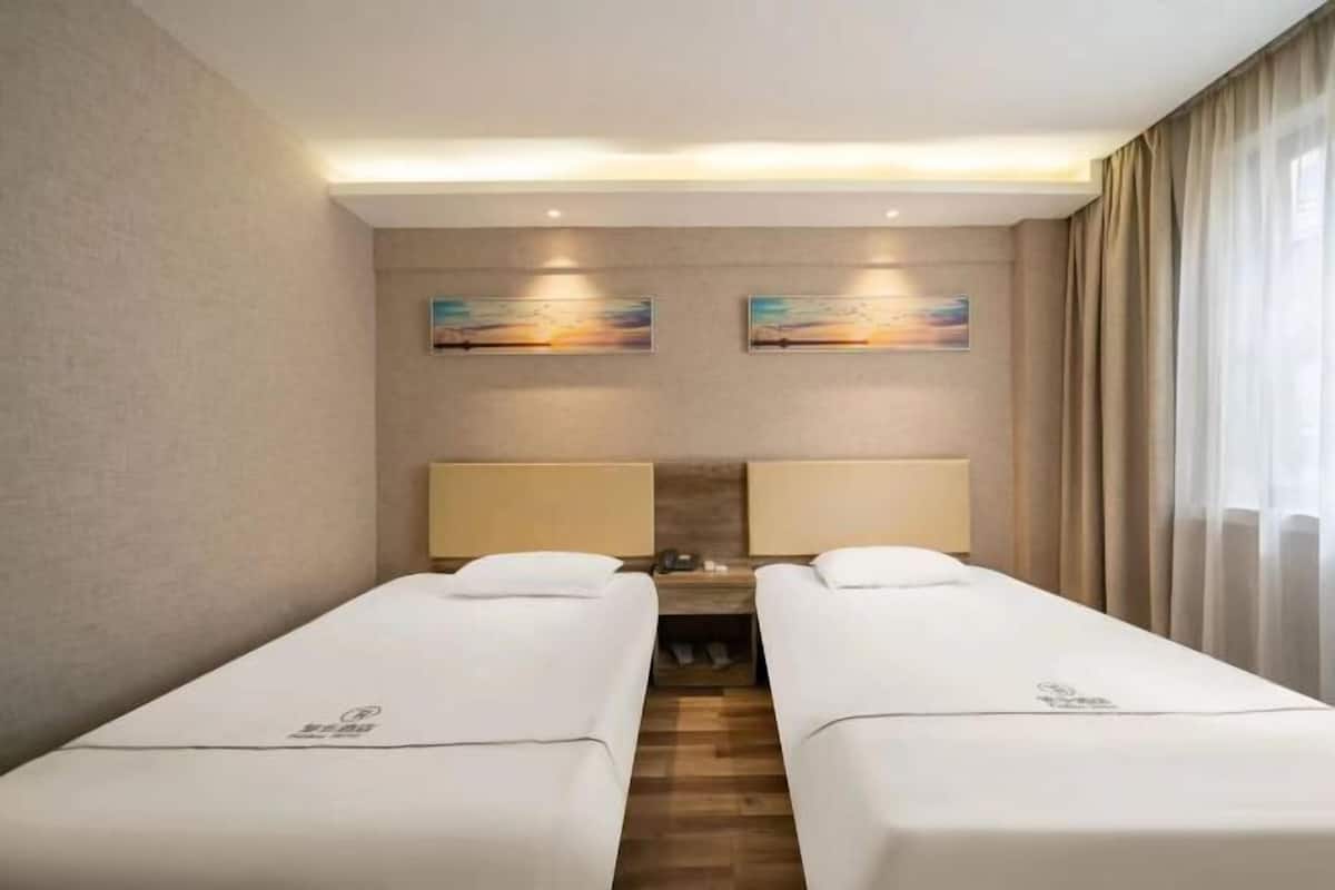 A hotel room with two single beds, a nightstand, and two wall-mounted lamps.