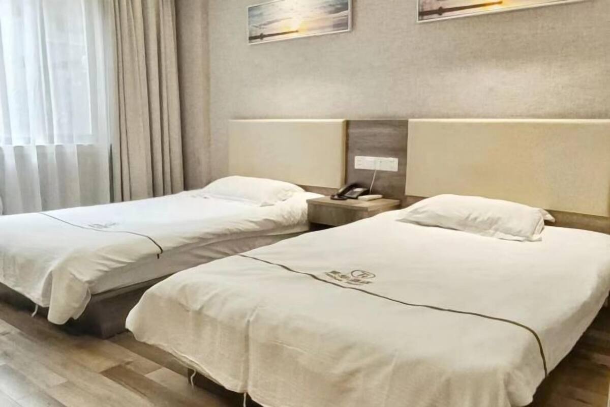 A hotel room with two beds, a nightstand with a phone, and a wall-mounted light.