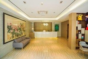 A hotel reception area with a reception desk, a sofa, a large painting, and a shelf with figurines. - Fanhua Hotel (Shanghai)