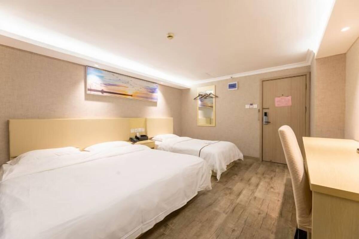 A hotel room with two beds, a desk, a chair, a mirror, and a painting on the wall.