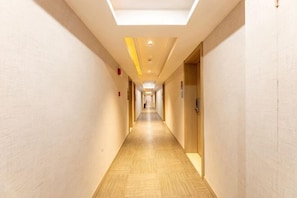A long, narrow hotel corridor with doors on both sides, a patterned floor, and a ceiling light fixture.