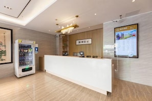 A reception area with a white reception desk, a vending machine, a digital display, and a wooden panel wall. - Fanhua Hotel (Shanghai)