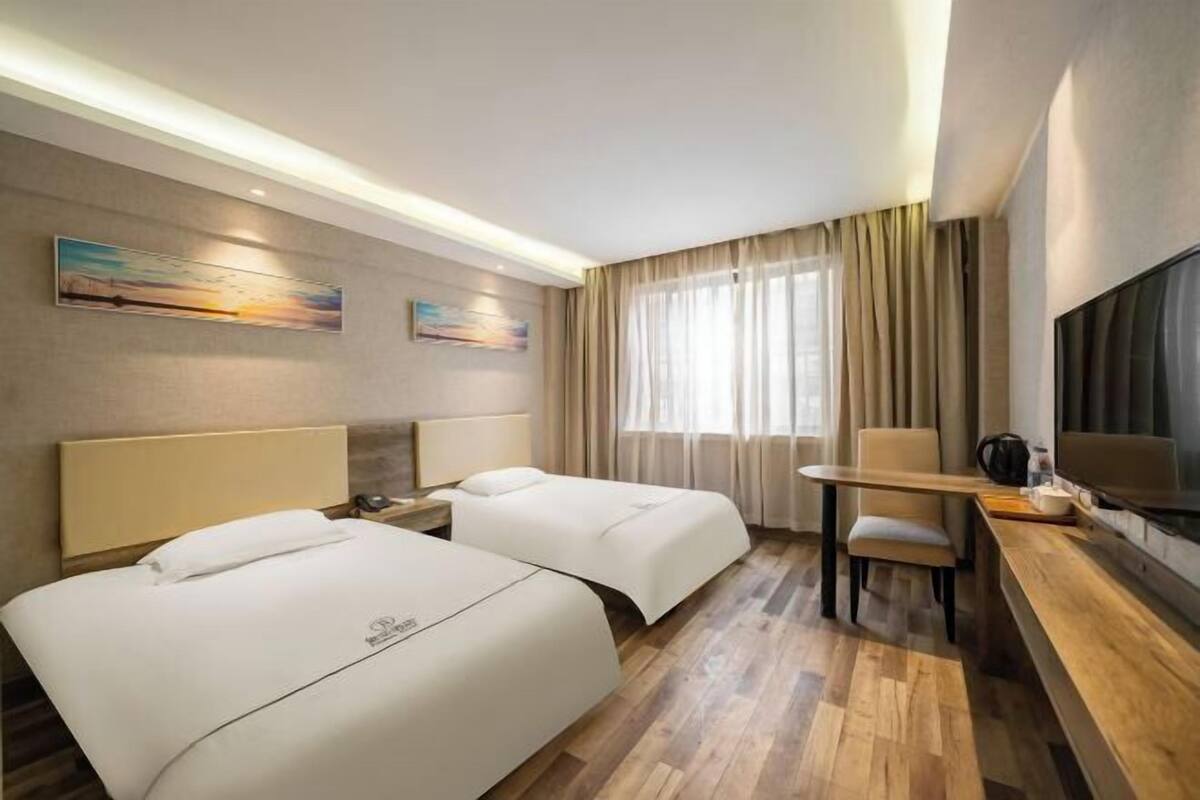 A hotel room with two beds, a desk, a chair, a TV, and artwork on the walls.