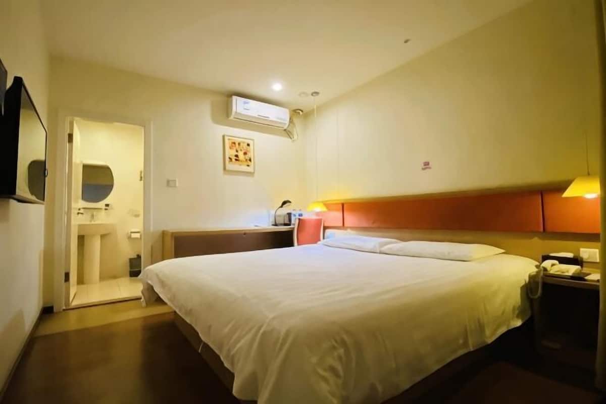 Una habitación de hotel con cama, mesita de noche, lámpara y aire acondicionado instalado en la pared.