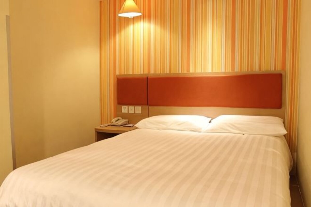 A hotel room with a bed, a nightstand with a phone, and a striped wall.