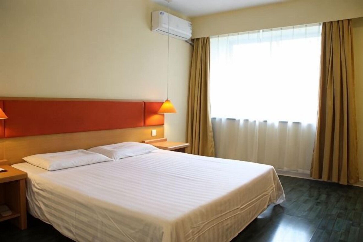 A hotel room with a large bed, two bedside tables, a headboard, and a window with curtains.