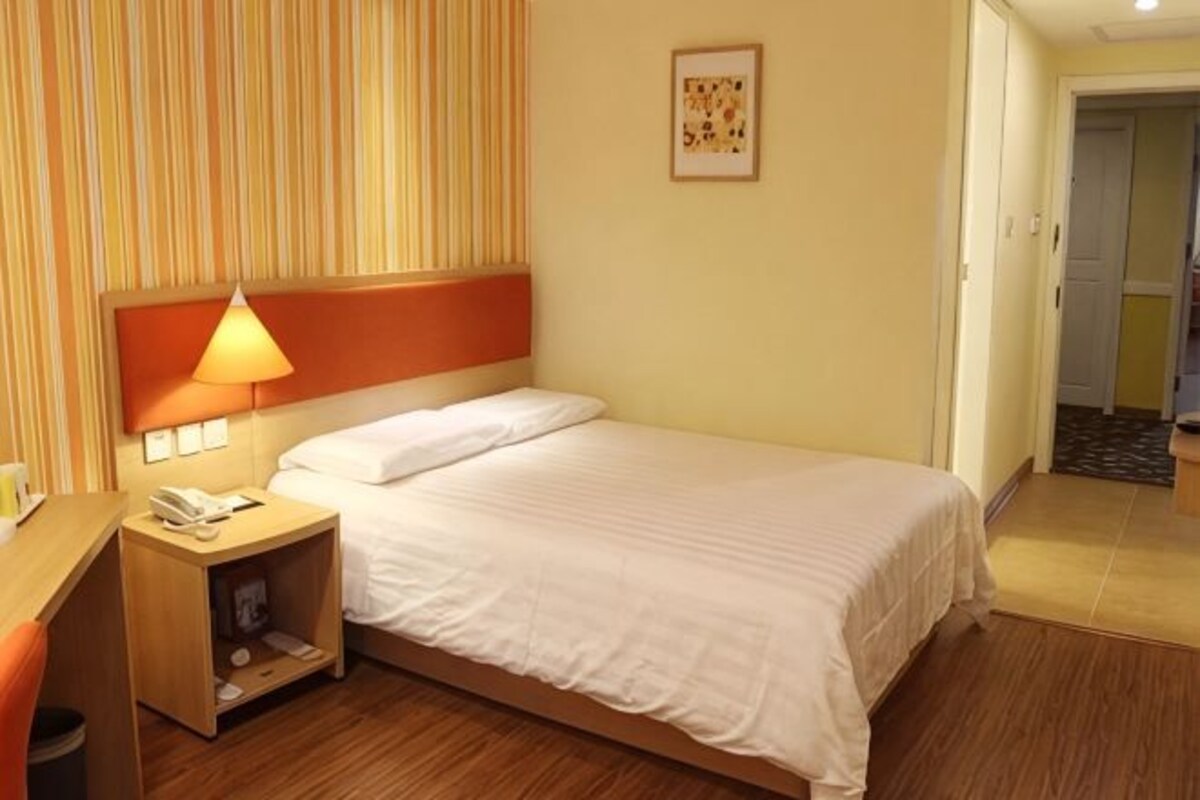 A hotel room with a bed, a nightstand with a lamp, a phone, and a picture on the wall.