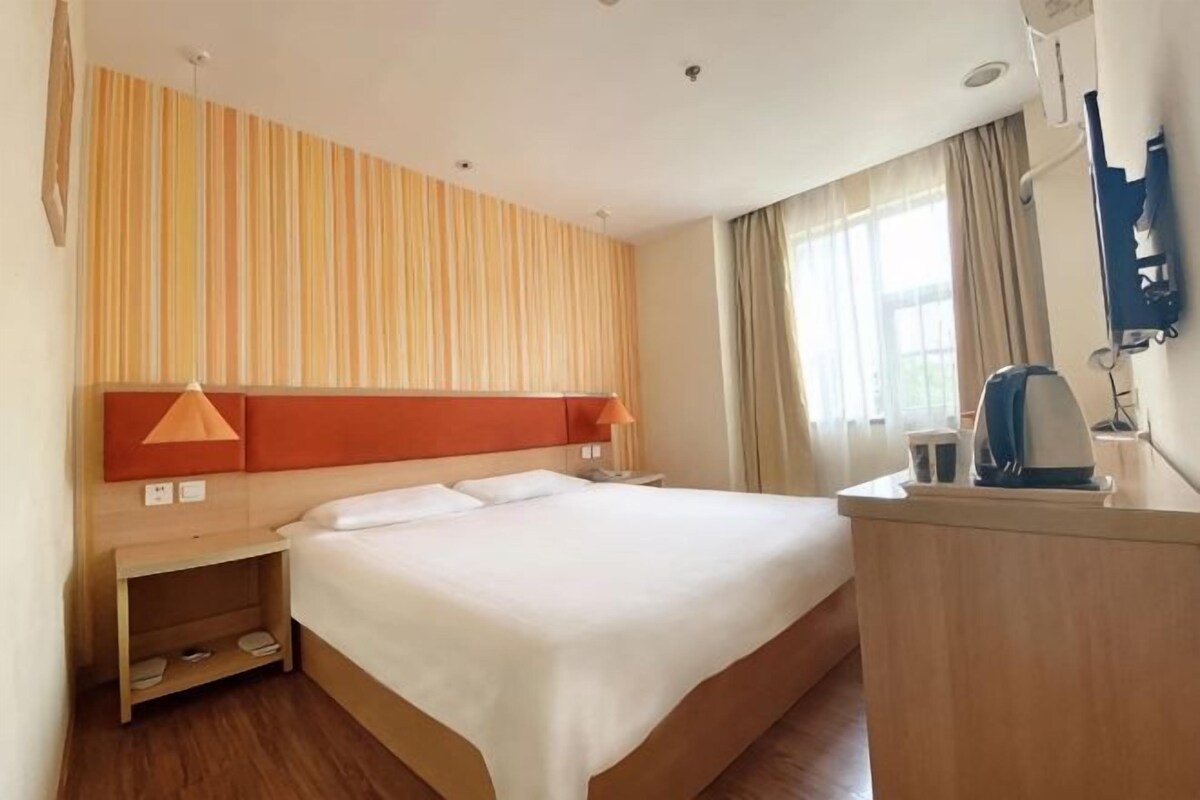 A hotel room with a large bed, a desk with a lamp, a small table, and a TV mounted on the wall.