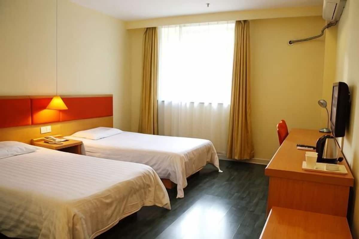 Habitación de hotel con dos camas, un escritorio, una silla, un televisor y una ventana con cortinas.