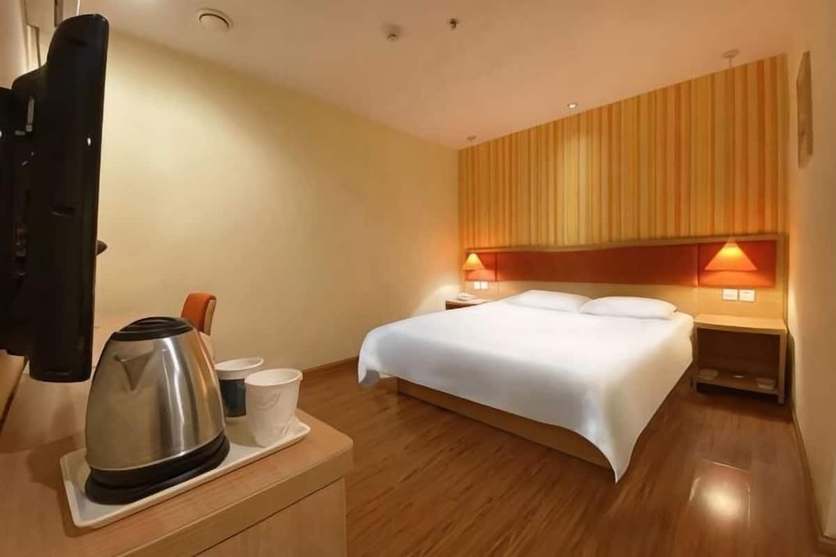 Una habitación de hotel con una cama, lámparas de noche, cafetera y televisión.