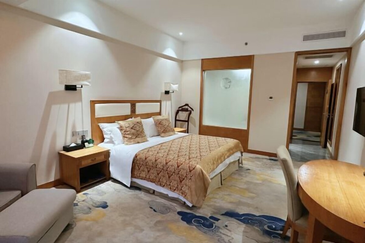 Una camera d'albergo con un letto, un comodino, una lampada, una sedia e un tavolino.