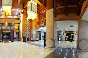 A spacious lobby with a grand staircase, a reception desk, and a decorative column.