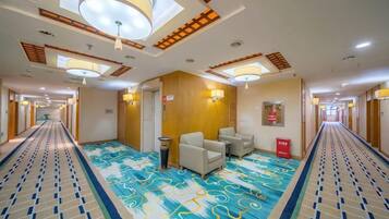 Pasillo de hotel con alfombra estampada, zona de estar y mostrador de recepción.