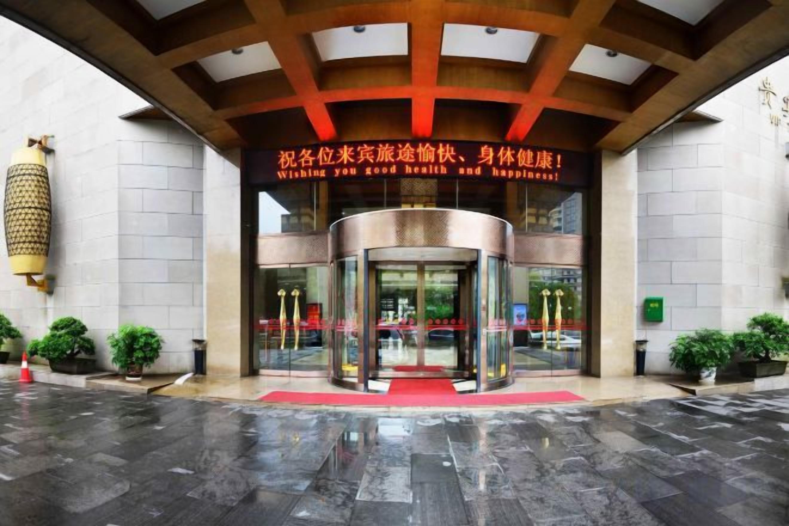 Entrada de hotel con puerta giratoria, alfombra roja y un letrero con caracteres chinos.
