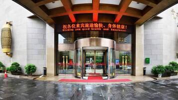 Entrada de hotel con puerta giratoria, alfombra roja y un letrero con caracteres chinos.