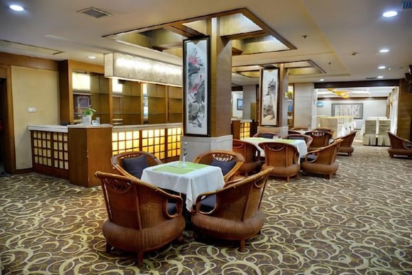 A hotel lobby with a reception desk, seating area with wicker chairs, and a patterned carpet.