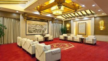 Un hall de hotel con alfombra roja, varias zonas de estar y un cuadro grande en la pared.