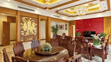 Un comedor de hotel con una mesa redonda, sillas de madera, un televisor y plantas decorativas.