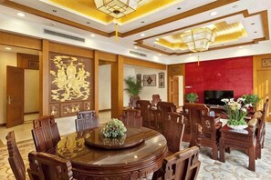 A hotel dining area with a round table, wooden chairs, a television, and decorative plants. - Xiangxi National Hotel (Xiangxi)