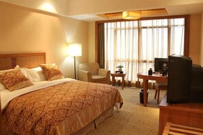 A hotel room with a large bed, a desk with a chair, a television, and a lamp.
