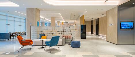 A modern lobby with a seating area, a reception desk, and a large screen displaying a cityscape.