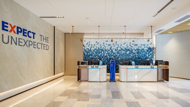 Ein moderner Empfangsbereich mit Marmorboden, einer Wand mit dem Schriftzug „EXPECT THE UNEXPECTED“ und einer Wand aus Mosaikfliesen hinter der Rezeption.