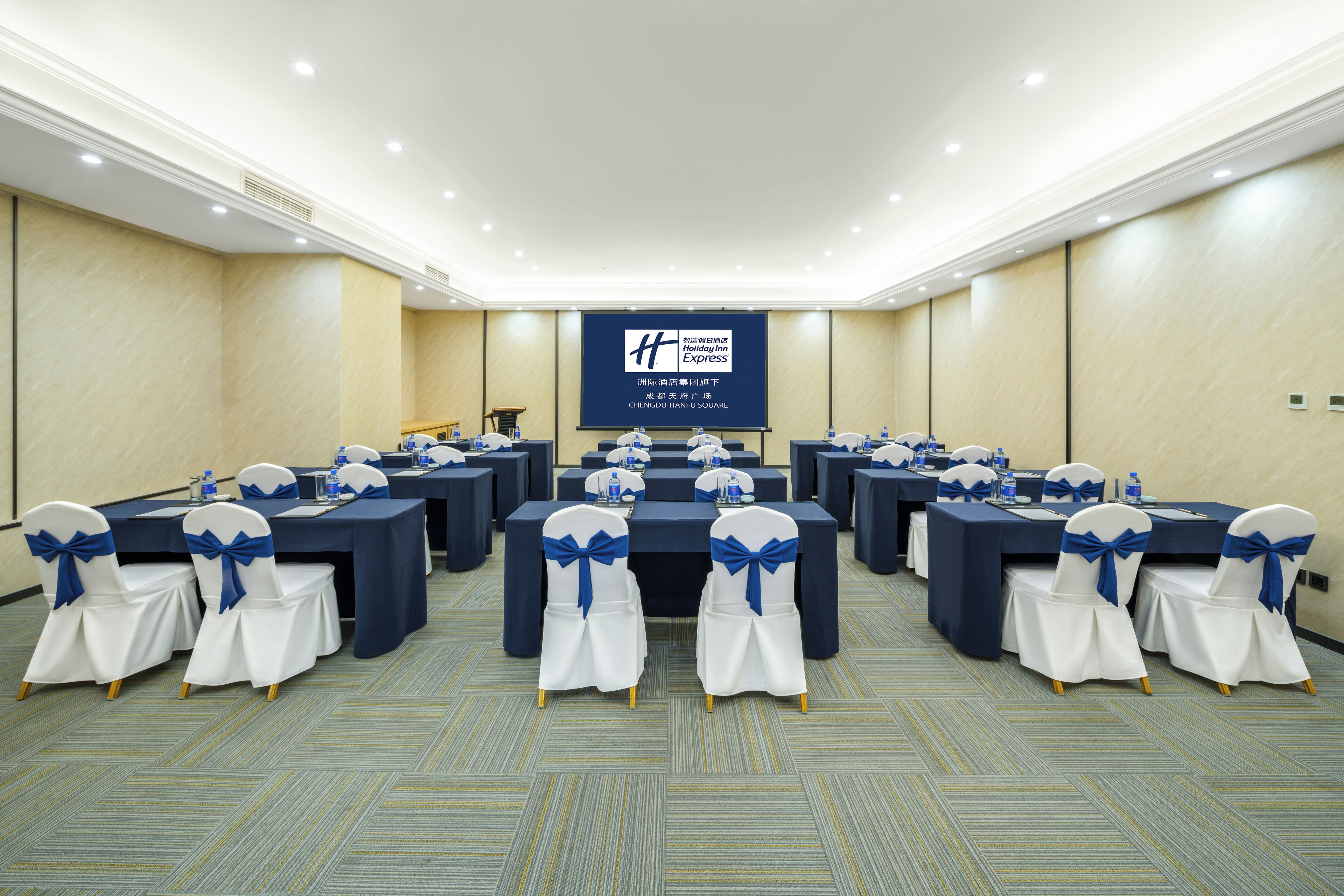 A conference room with tables and chairs, a projection screen, and a carpeted floor.