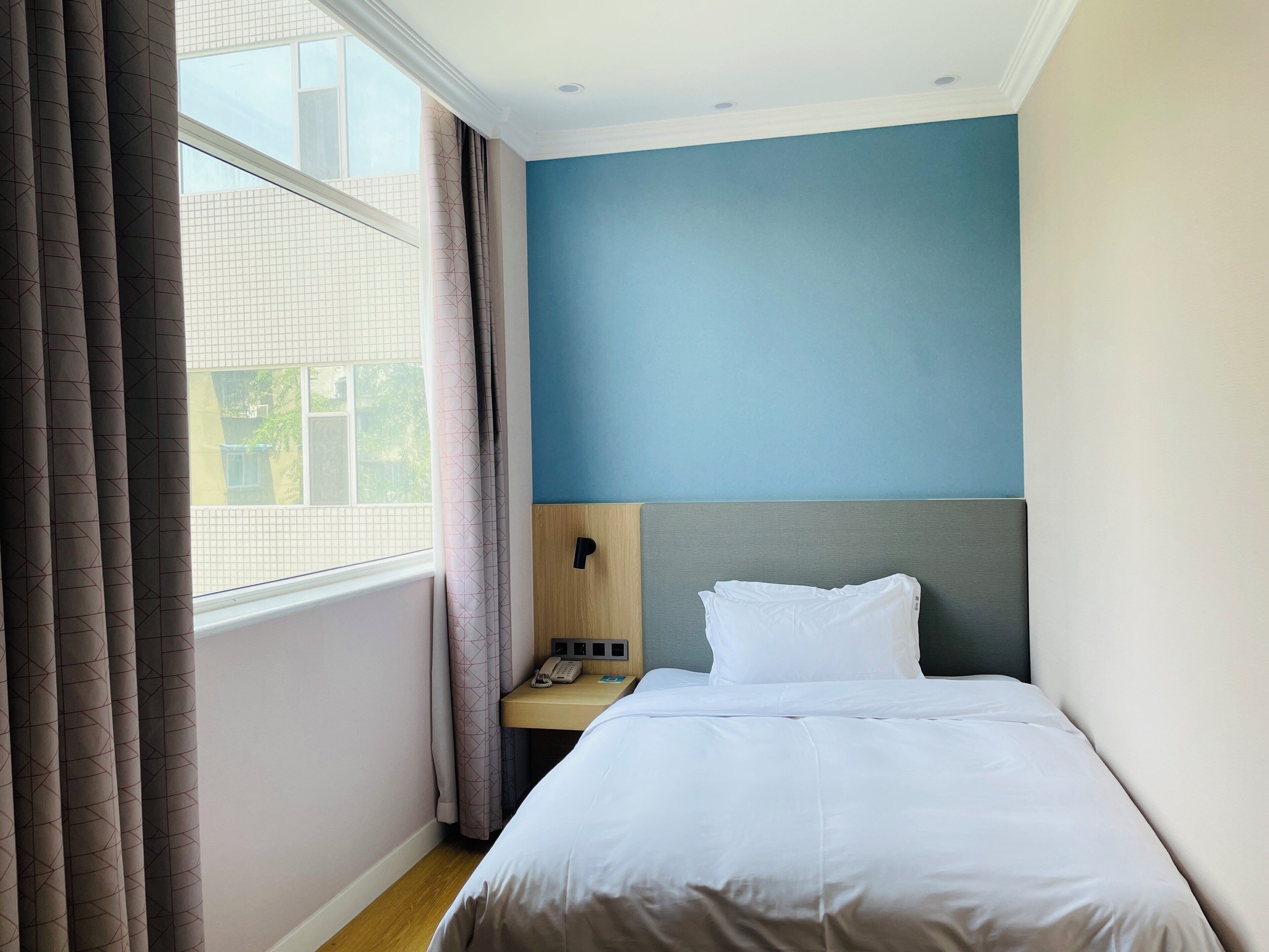 Een hotelkamer met een bed, een nachtkastje met telefoon, en een raam met gordijnen.