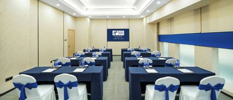 A conference room with multiple tables, chairs, and a projection screen.