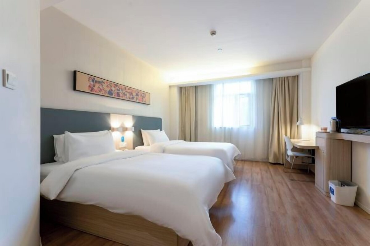 Une chambre d’hôtel avec deux lits, un bureau, une télévision et une fenêtre avec des rideaux.