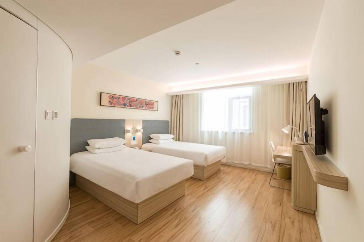 Une chambre d’hôtel avec deux lits, un bureau, une télévision et une fenêtre avec des rideaux.