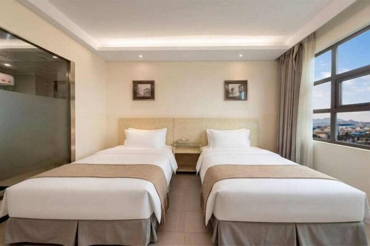 Habitación de hotel con dos camas, un ventanal grande y vistas a la ciudad.