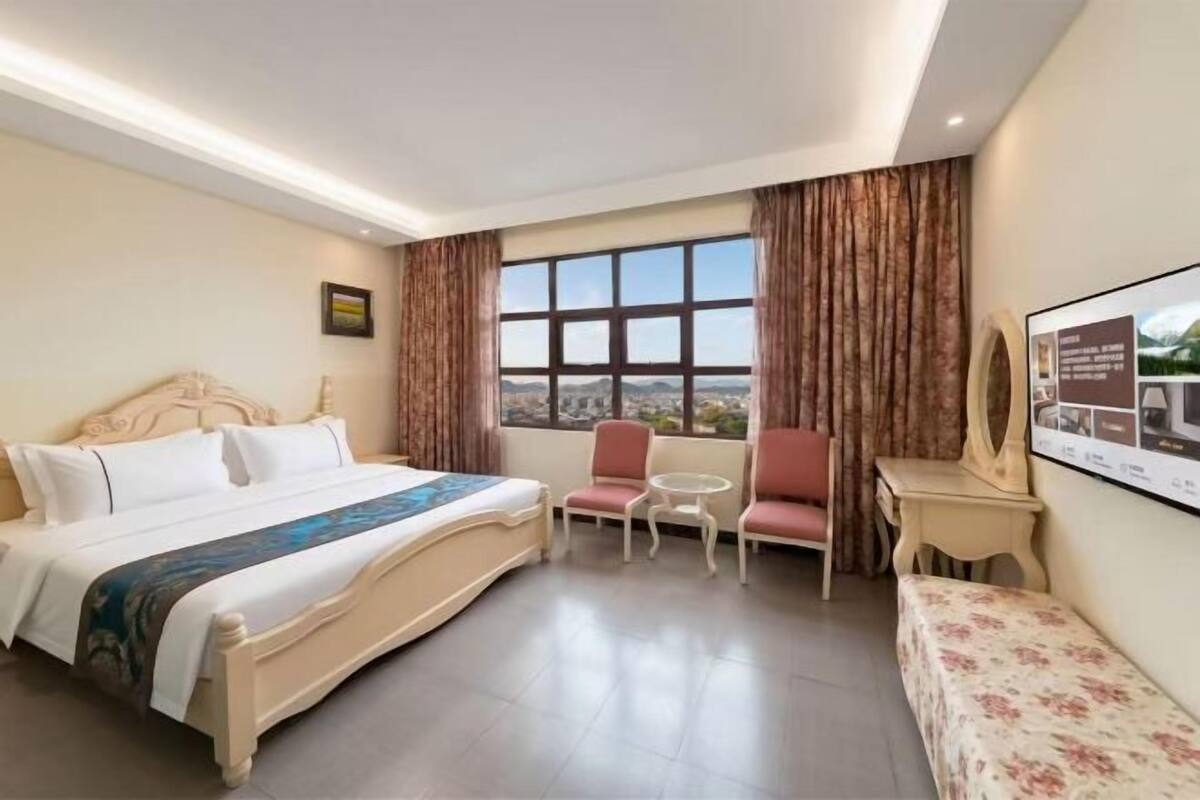 Una habitación de hotel con una cama, una mesita, una silla y vistas a través de un ventanal grande.