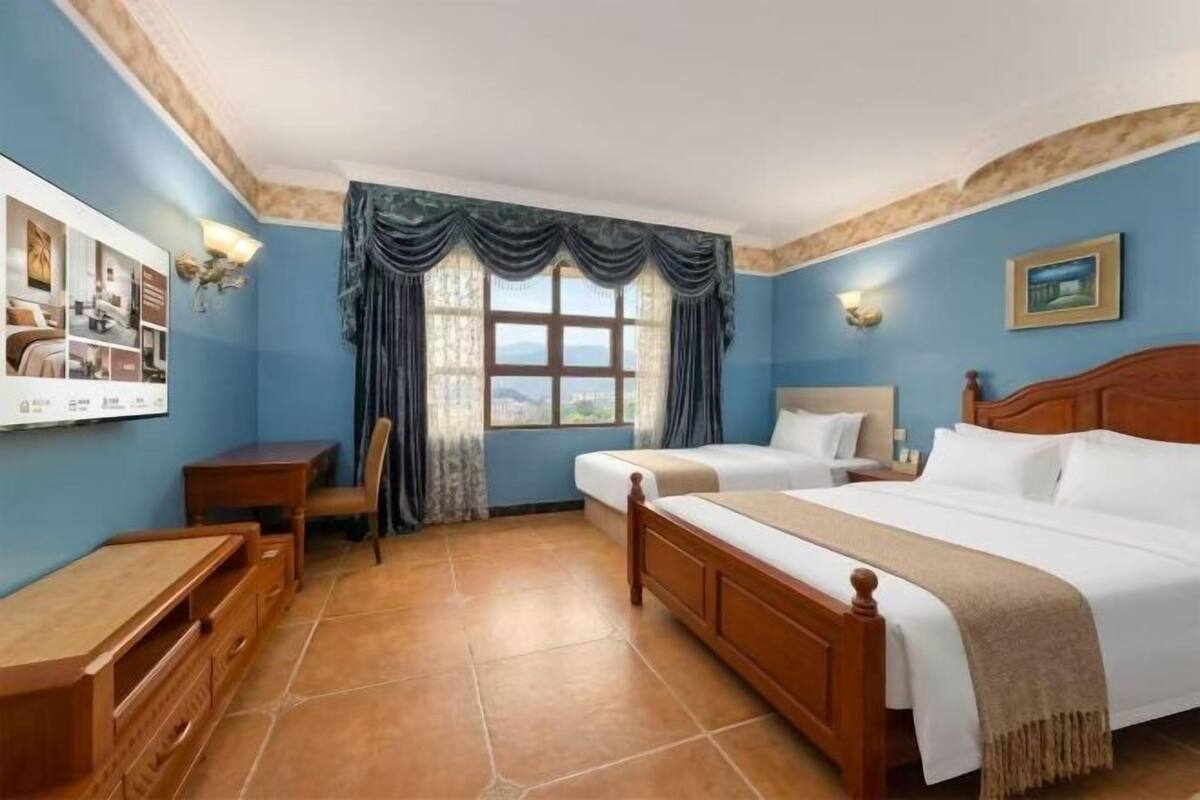 Un dormitorio con cama, escritorio, silla y ventana con cortinas.